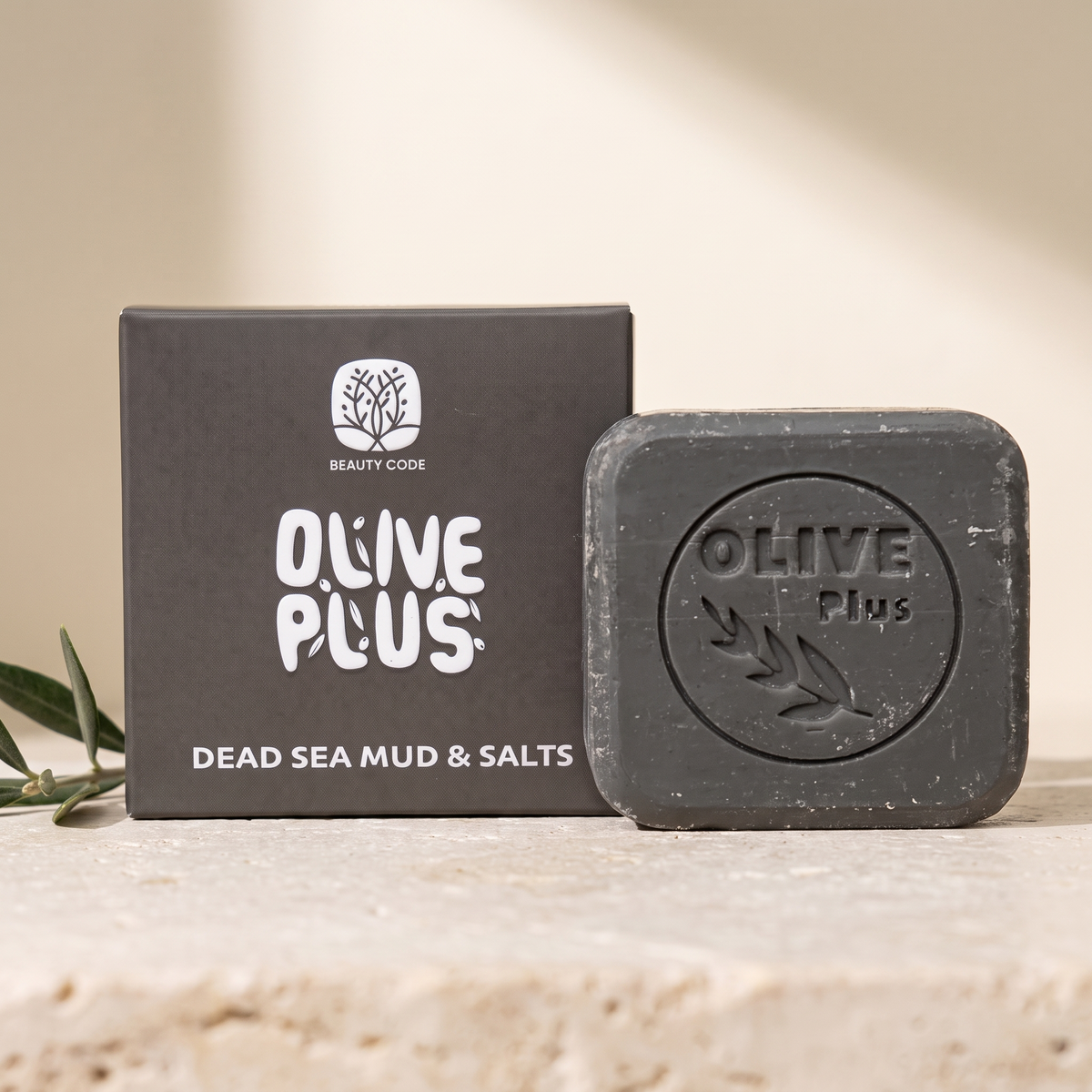 Olive Plus Dead Sea Mud & Salts soap bar and original charcoal packaging on warm limestone